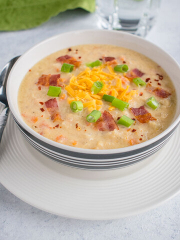 bowl of soup with cheddar, bacon and green onions and spoon
