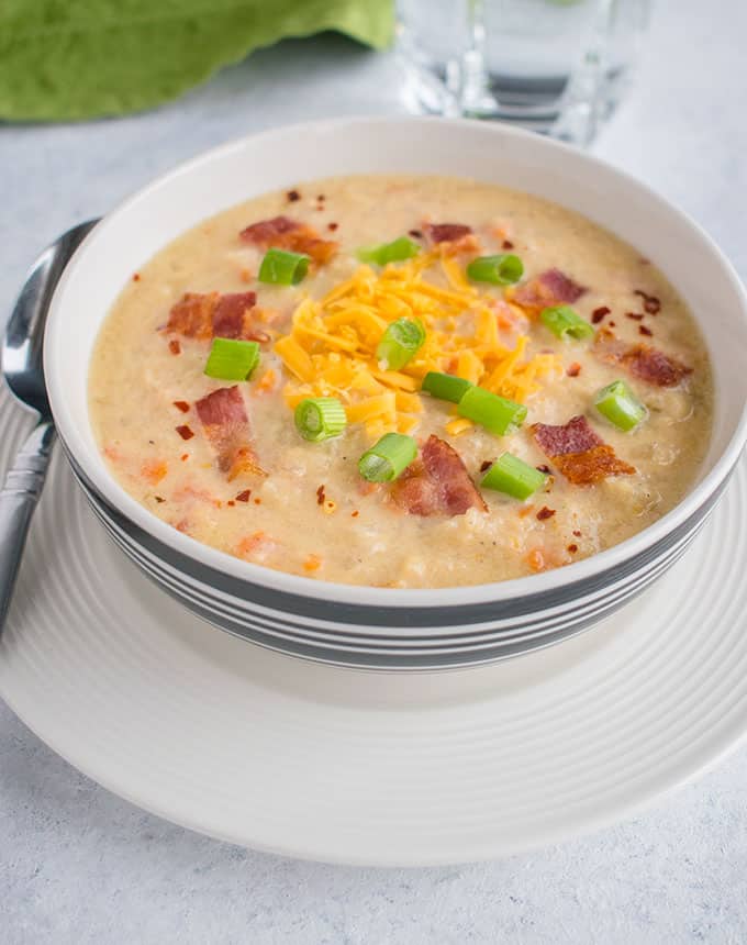bowl of soup with cheddar, bacon and green onions and spoon