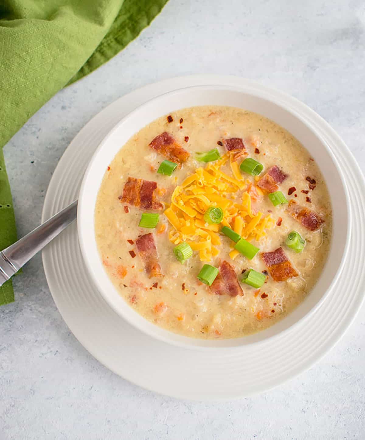 bowl of soup with cheddar, bacon, green onions, spoon and green napkin