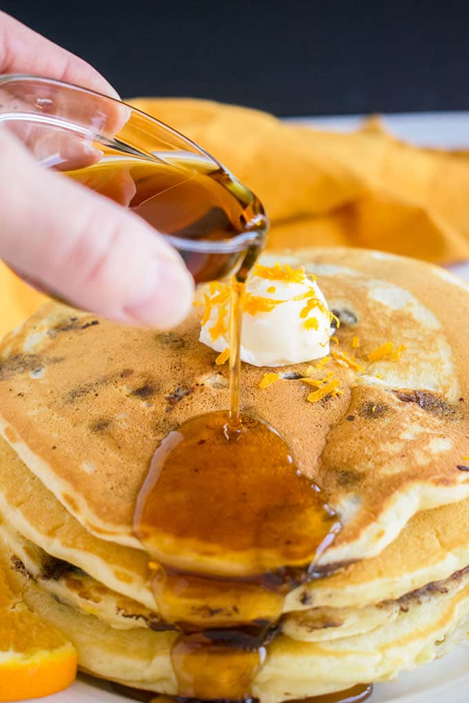 pouring syrup on stack of chocolate chip pancakes