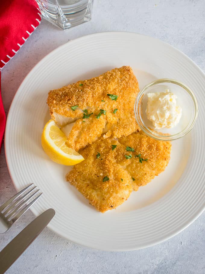 breaded fish on a plate with lemon and mayo