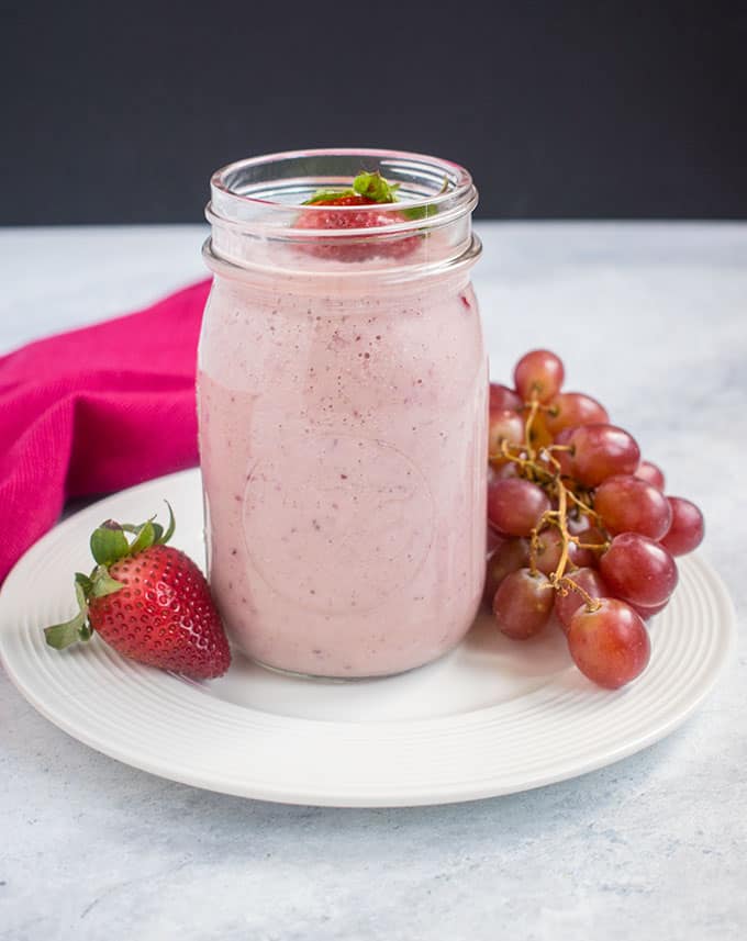 pink smoothie in jar, strawberries, grapes, pink napkin, white dish