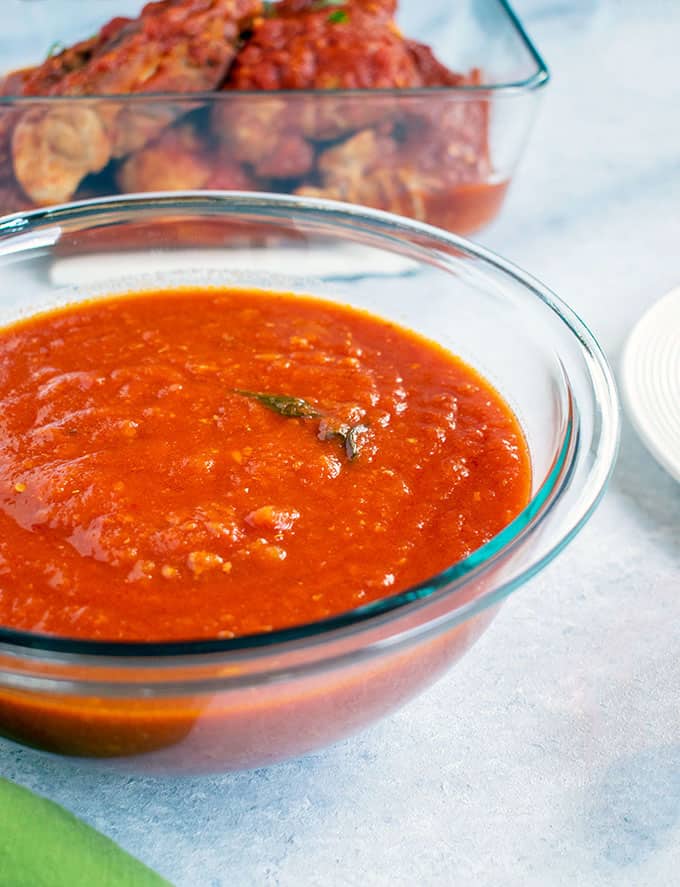 bowl of tomato sauce, meat in background