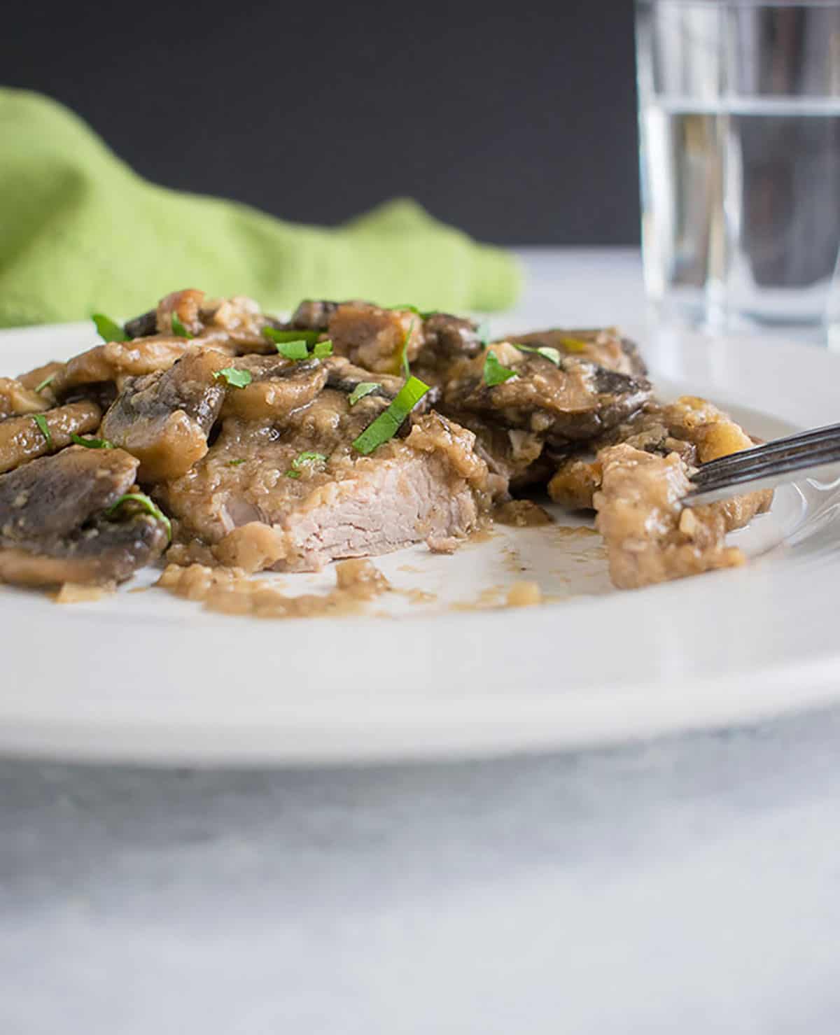 plate of cooked pork and mushrooms with forkful of meat