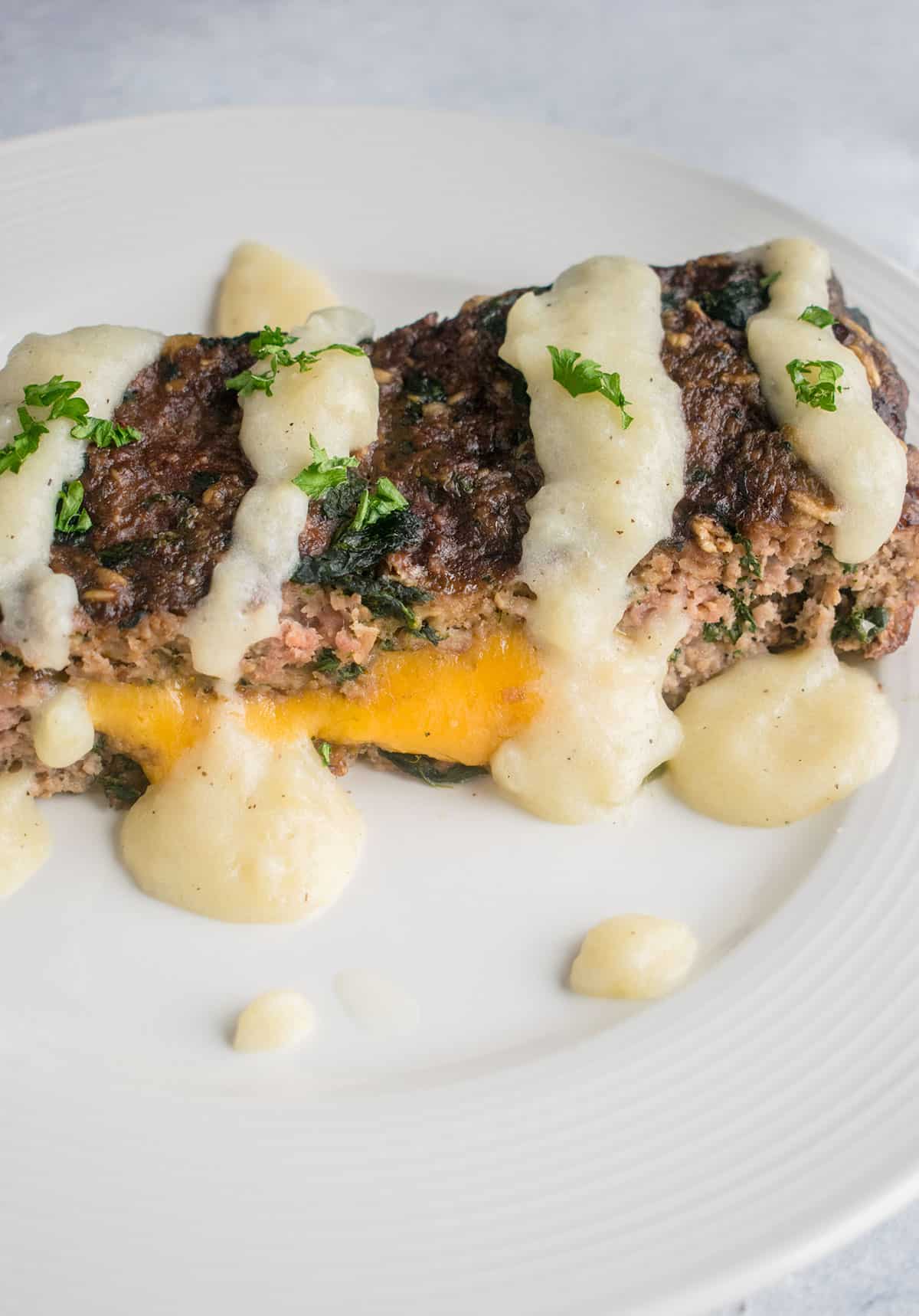 closeup of cheesy meatloaf with potato soup gravy on plate