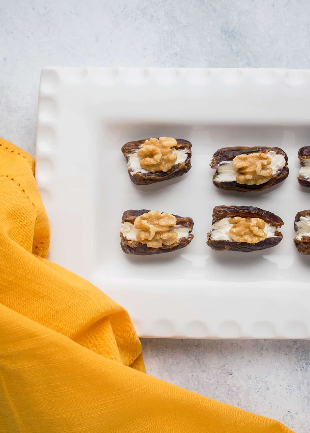 dates with cream cheese and walnuts in white platter, gold napkin