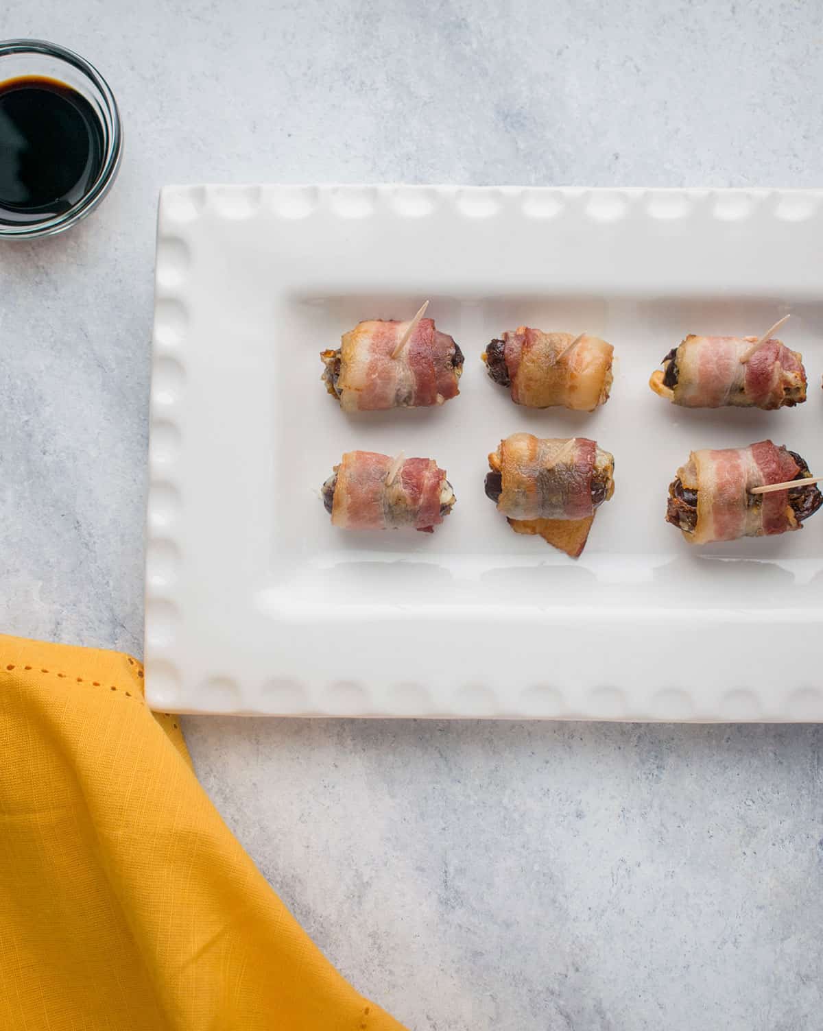 bacon-wrapped appetizers on white platter with little bowl of soy sauce