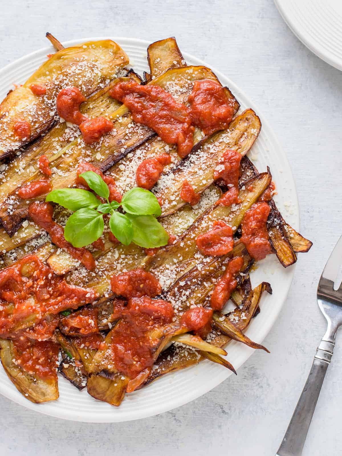 eggplant planks with tomato sauce and Parmesan on white plate with basil
