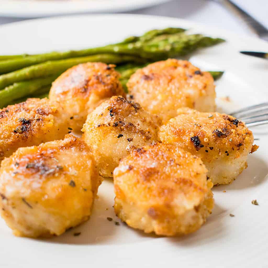 closeup of breaded broiled scallops with asparagus