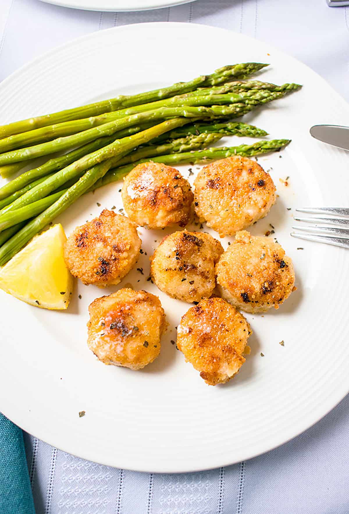 breaded scallops on white plate with lemon and asparagus