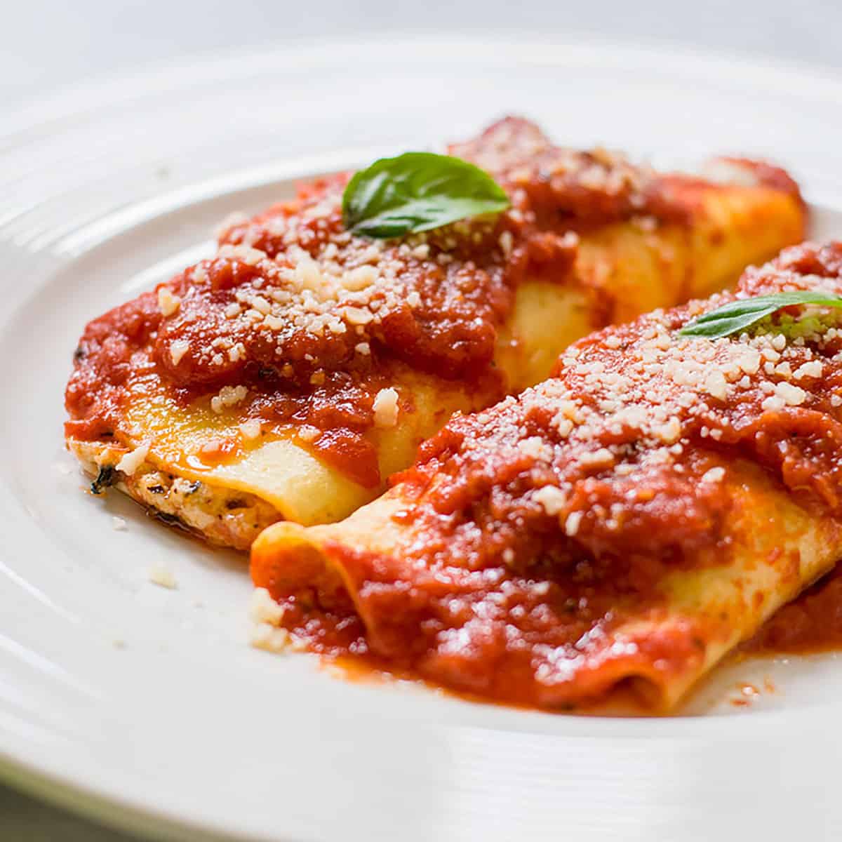 closeup of manicotti on white plate with sauce and basil leaves