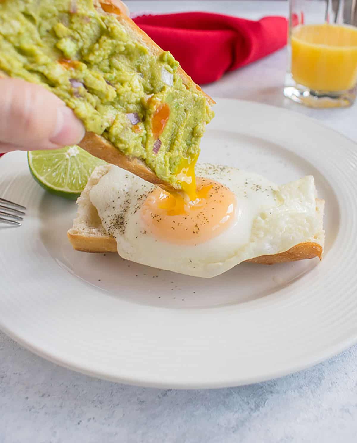 dipping guacamole toast in yolk of basted egg 