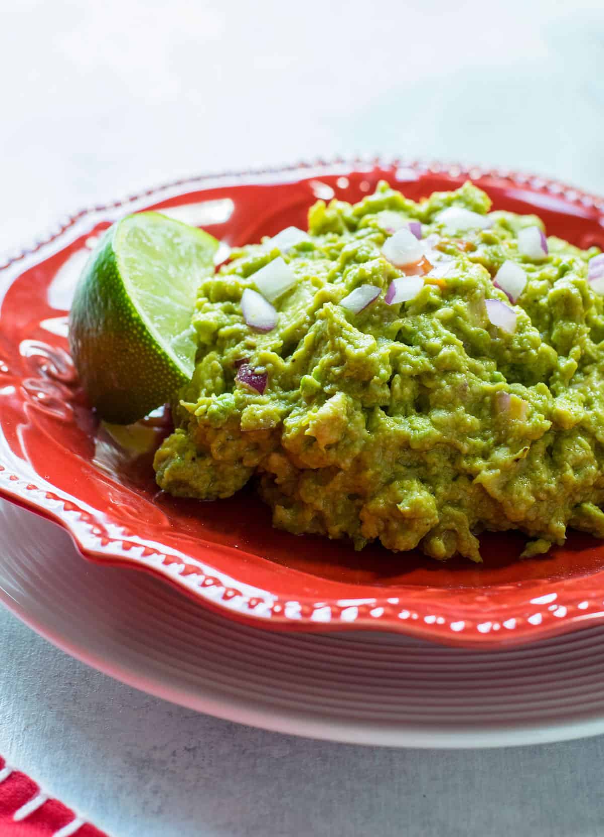 closeup of guacamole with lime and red onions on a red plate