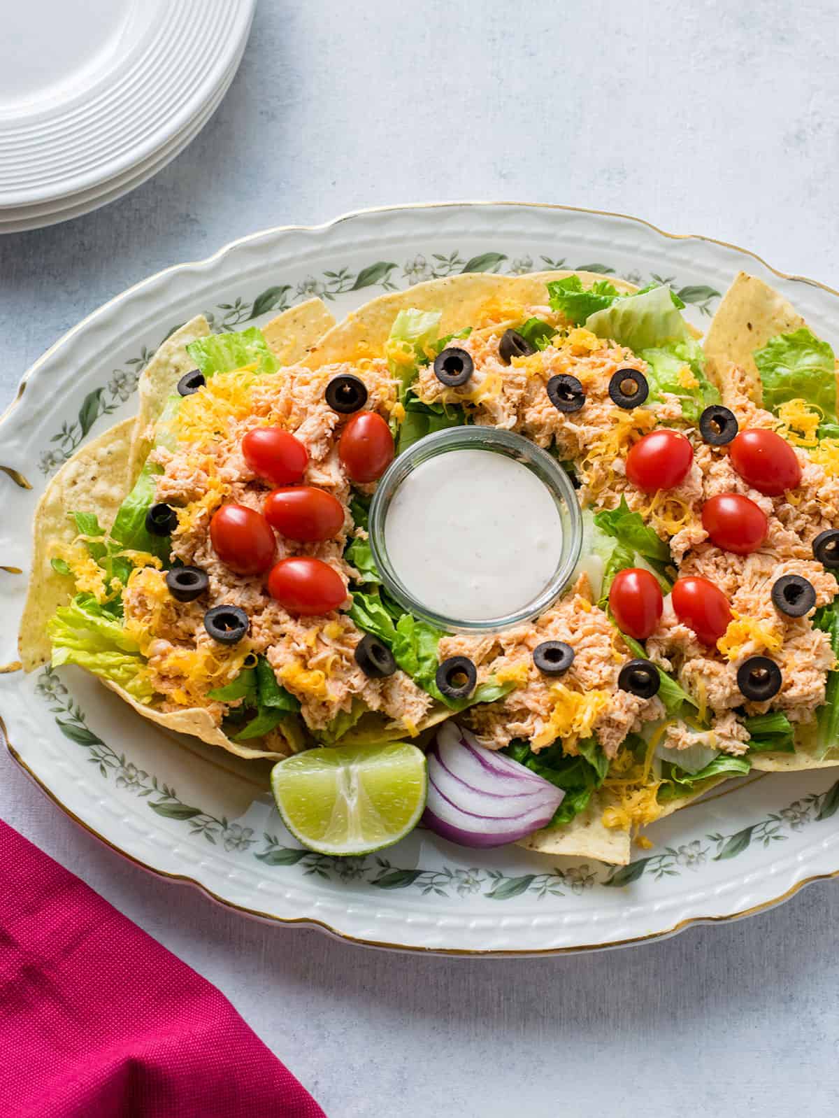 platter of shredded chicken on lettuce and nachos with olives, cheese, tomatoes, onion, lime, Ranch