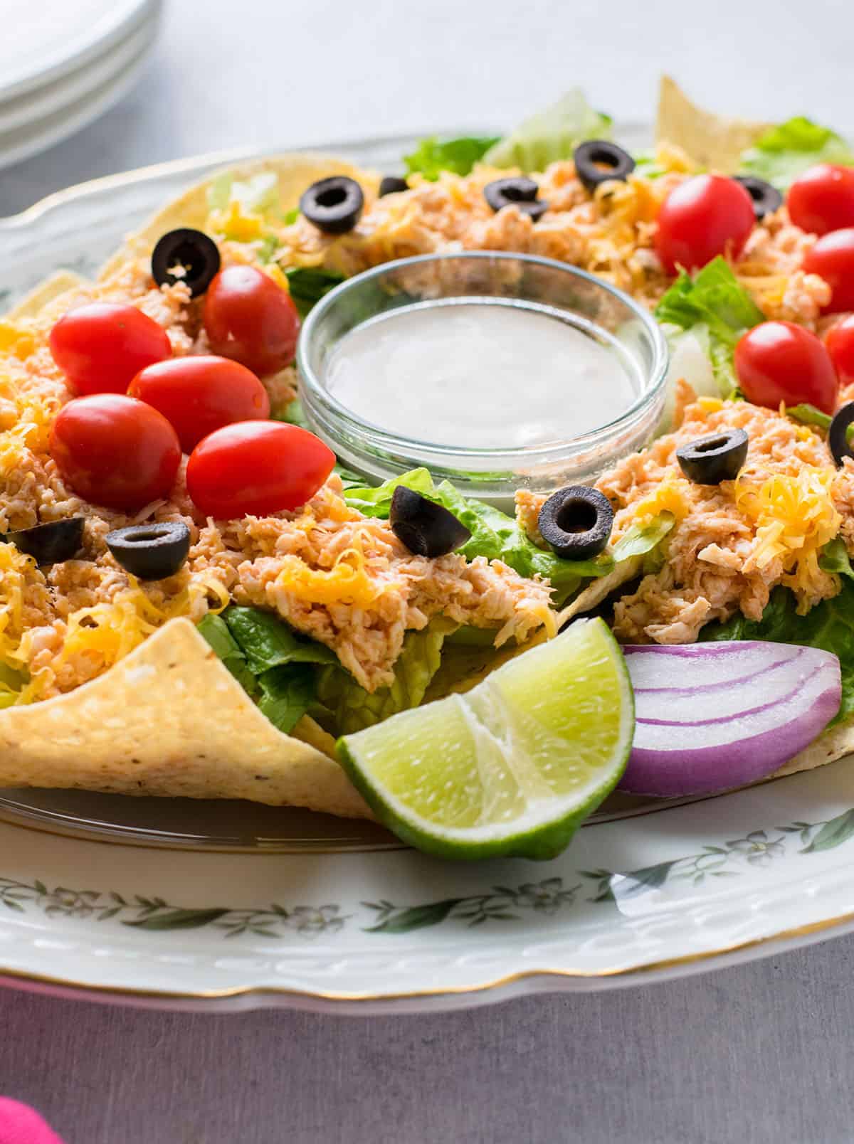 closeup of shredded chicken with lettuce, nachos, olives, tomatoes, ranch dressing, lime, cheese