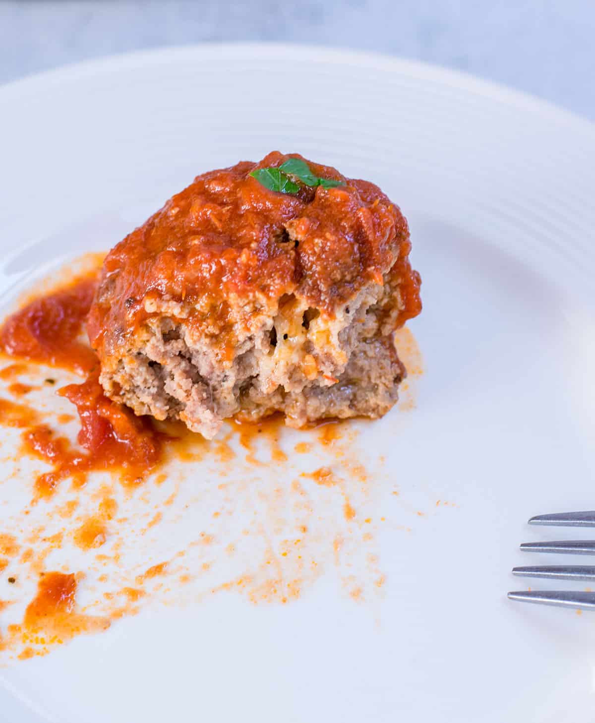 cut open meatball with tomato sauce on white plate