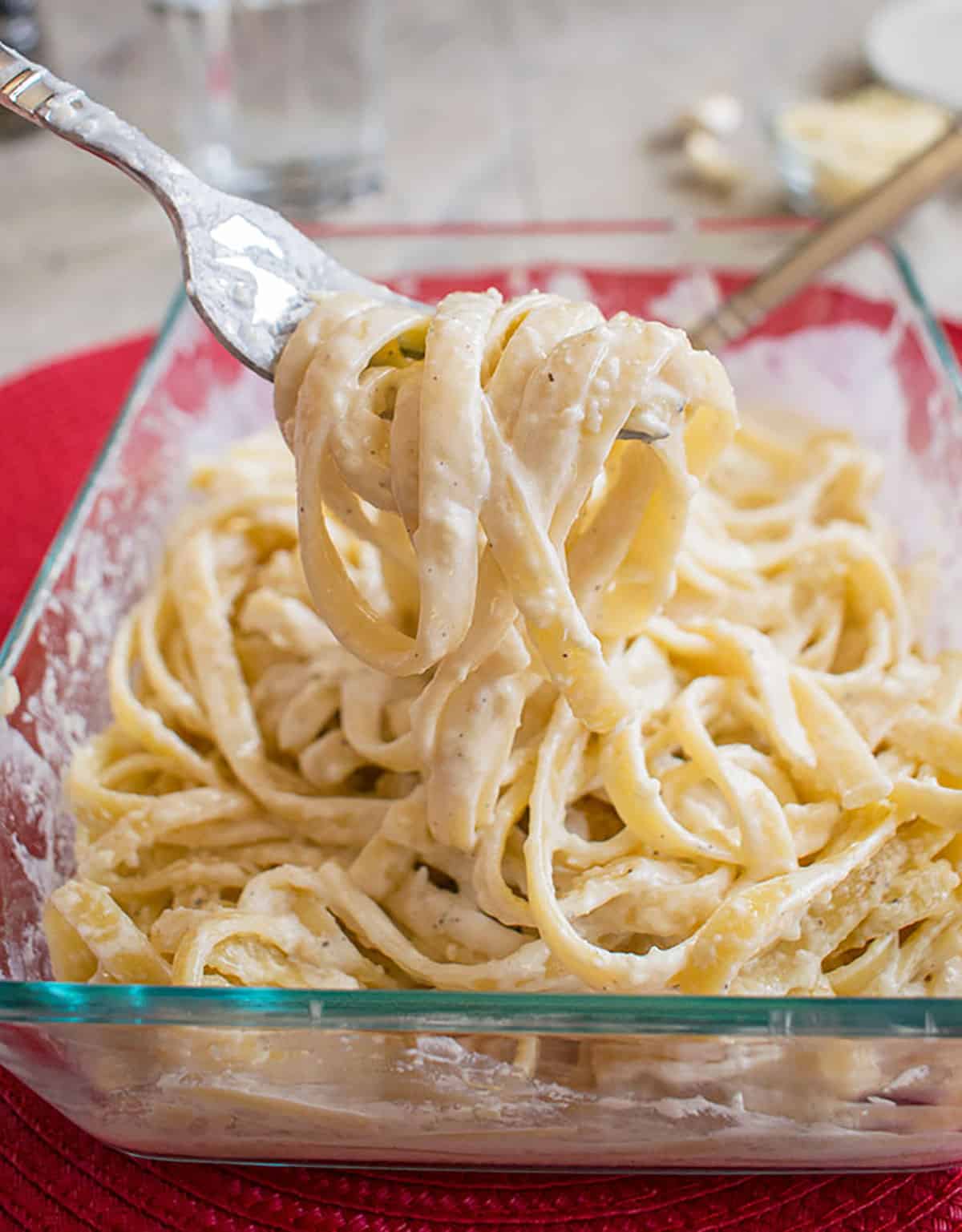 closeup of fettuccine alfredo in glass pan with forkful lifted up