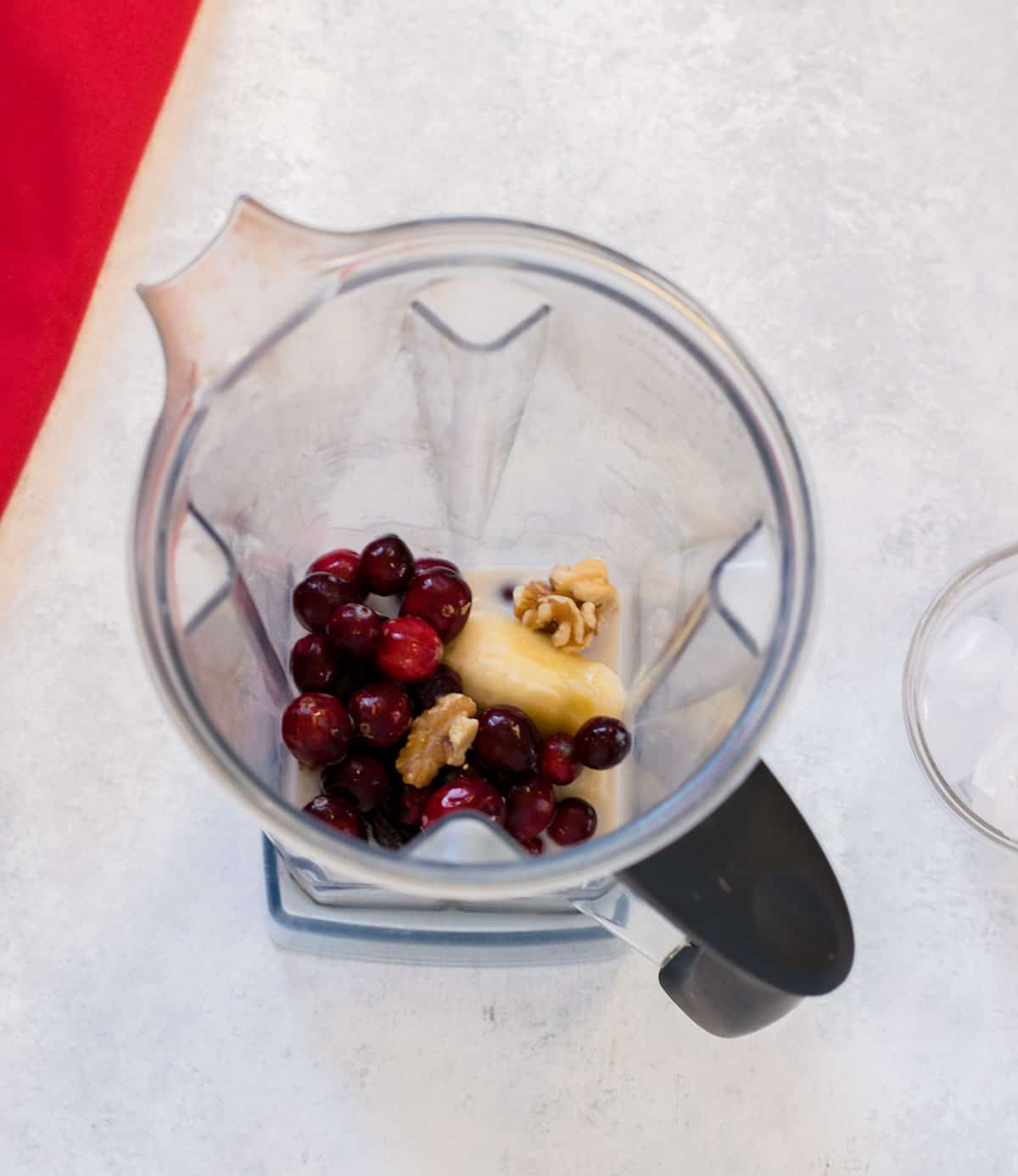 overhead view of blender containing cranberries, banana, walnuts, milk 