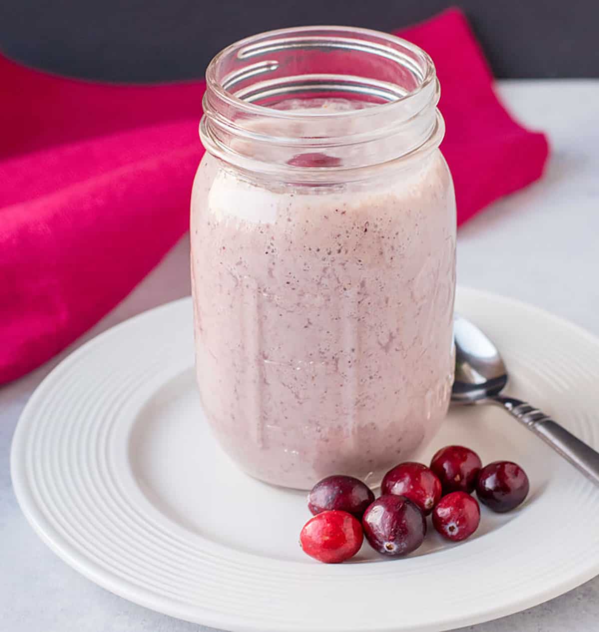 cranberry smoothie in mason jar on plate with spoon, napkin