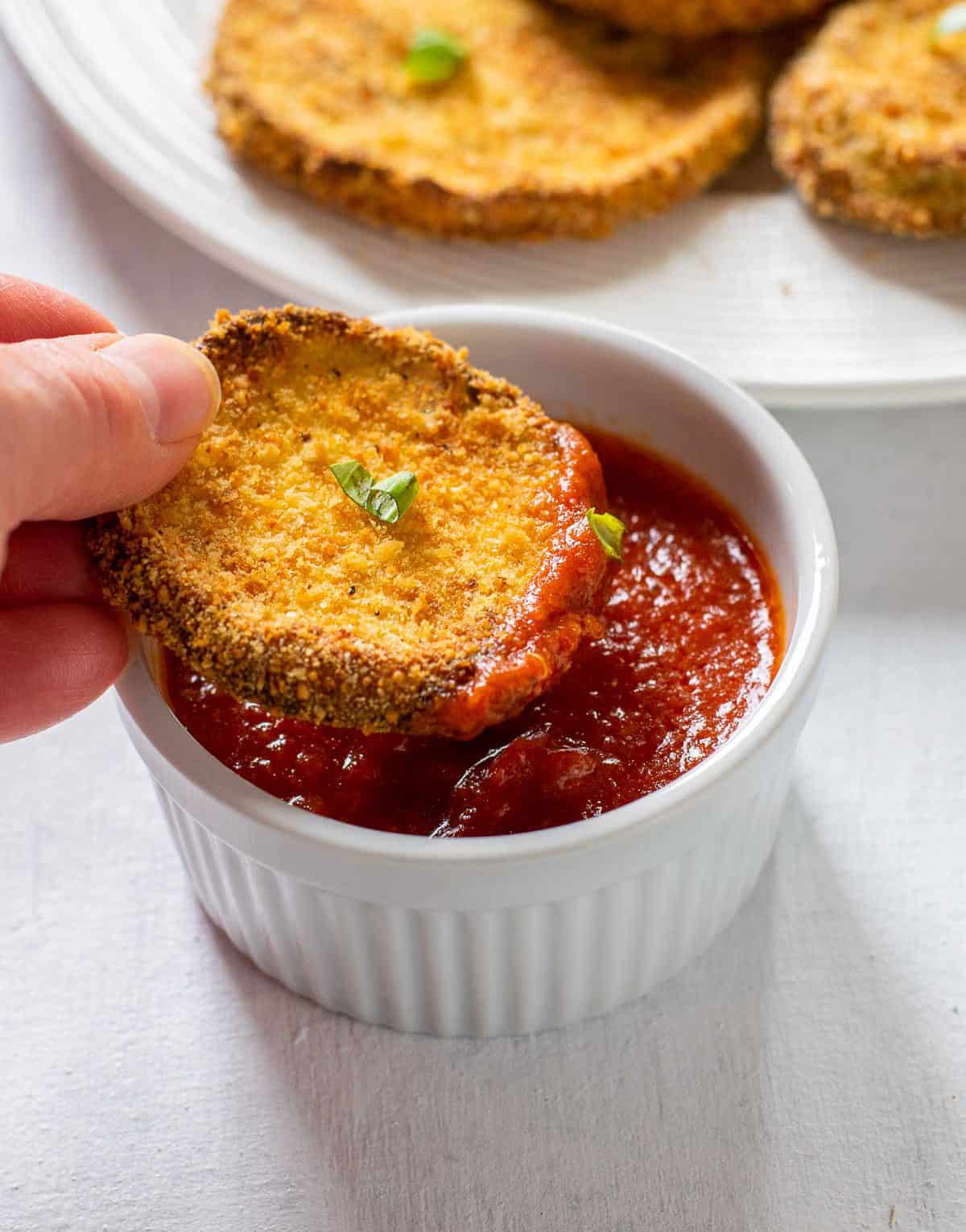 holding slice of breaded eggplant dipped in tomato sauce.