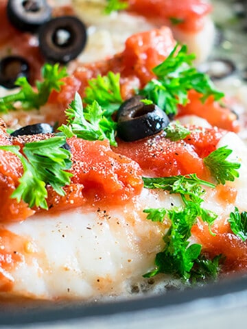 fish with tomatoes, olives, parsley in pan