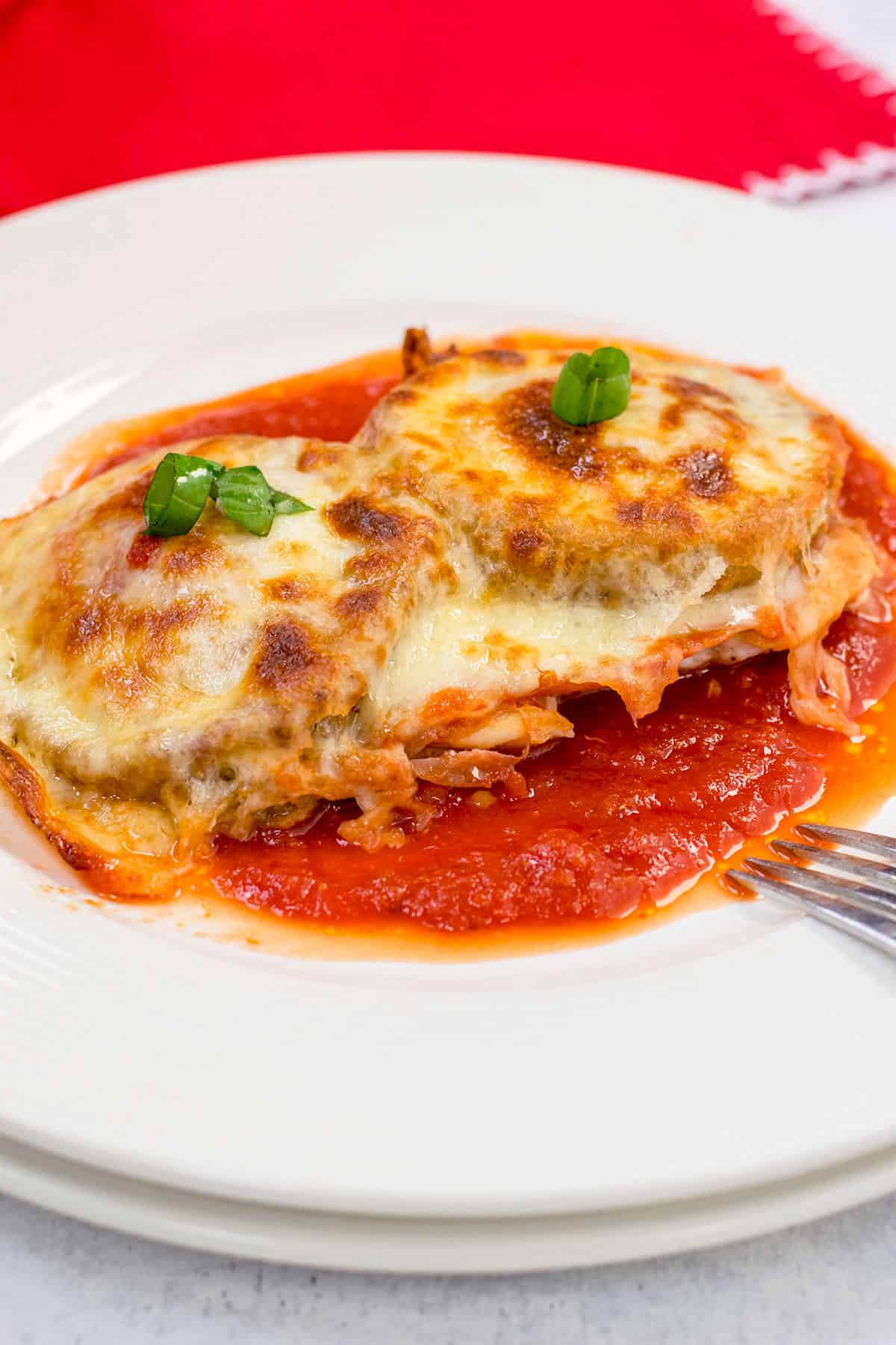 chicken with eggplant and melted cheese on plate of tomato sauce