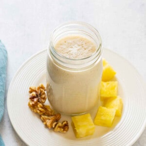 pineapple smoothie with coconut in jar on plate with walnuts and pineapple chunks