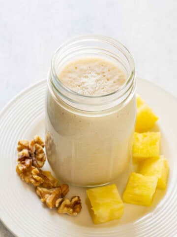 pineapple smoothie with coconut in jar on plate with walnuts and pineapple chunks