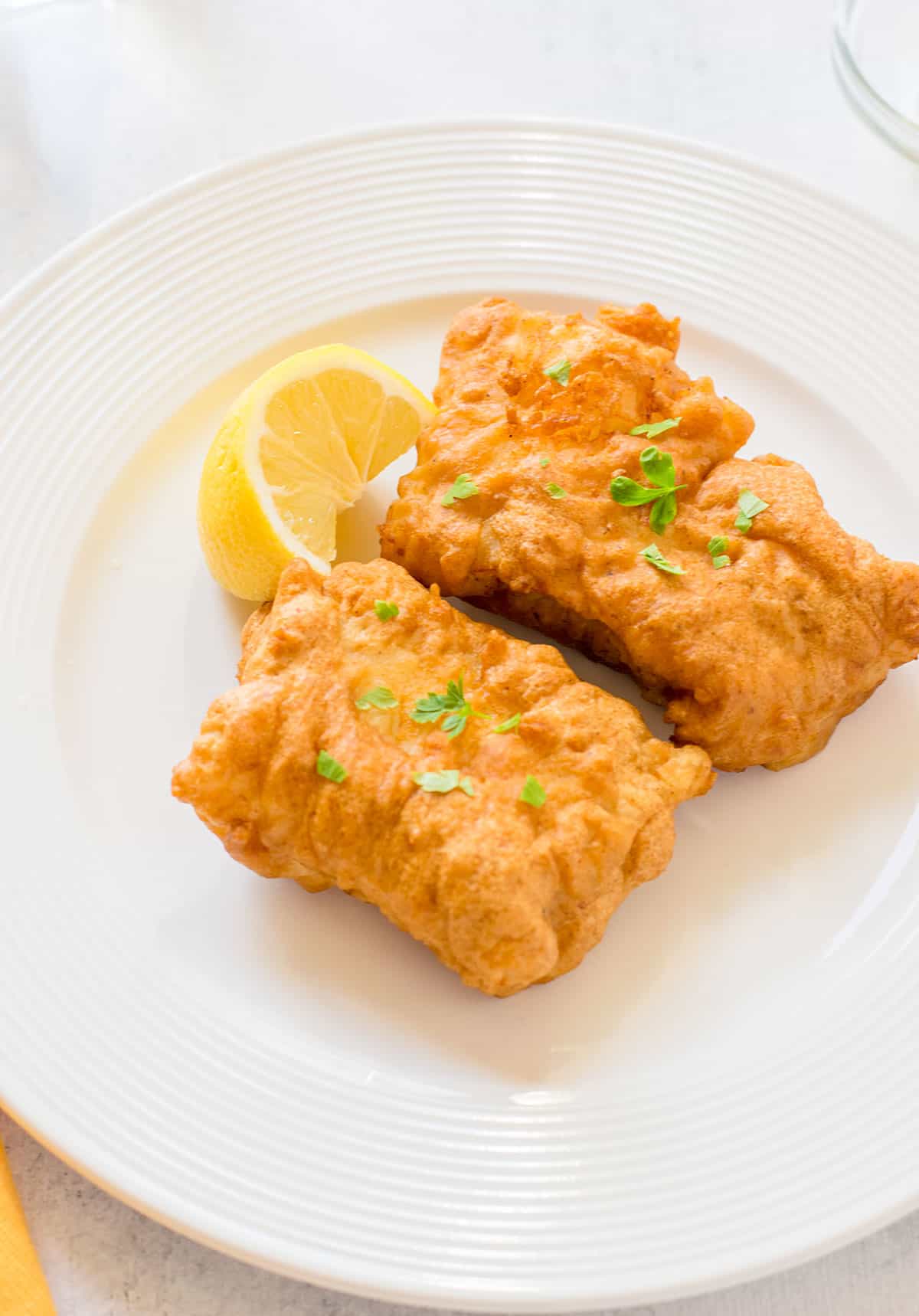 two pieces of deep fried fish on plate with lemon