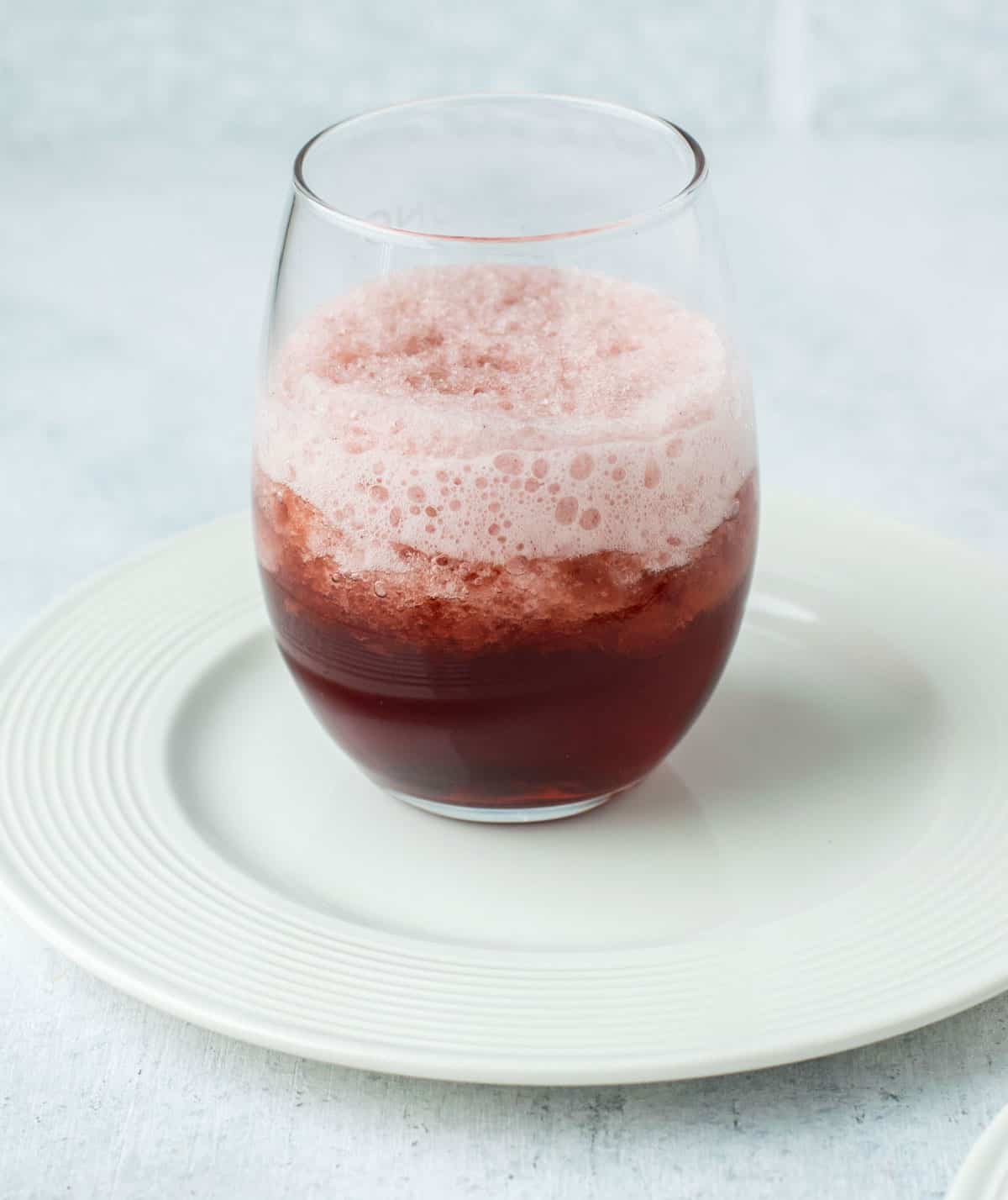 red wine slushie in glass on white plate.