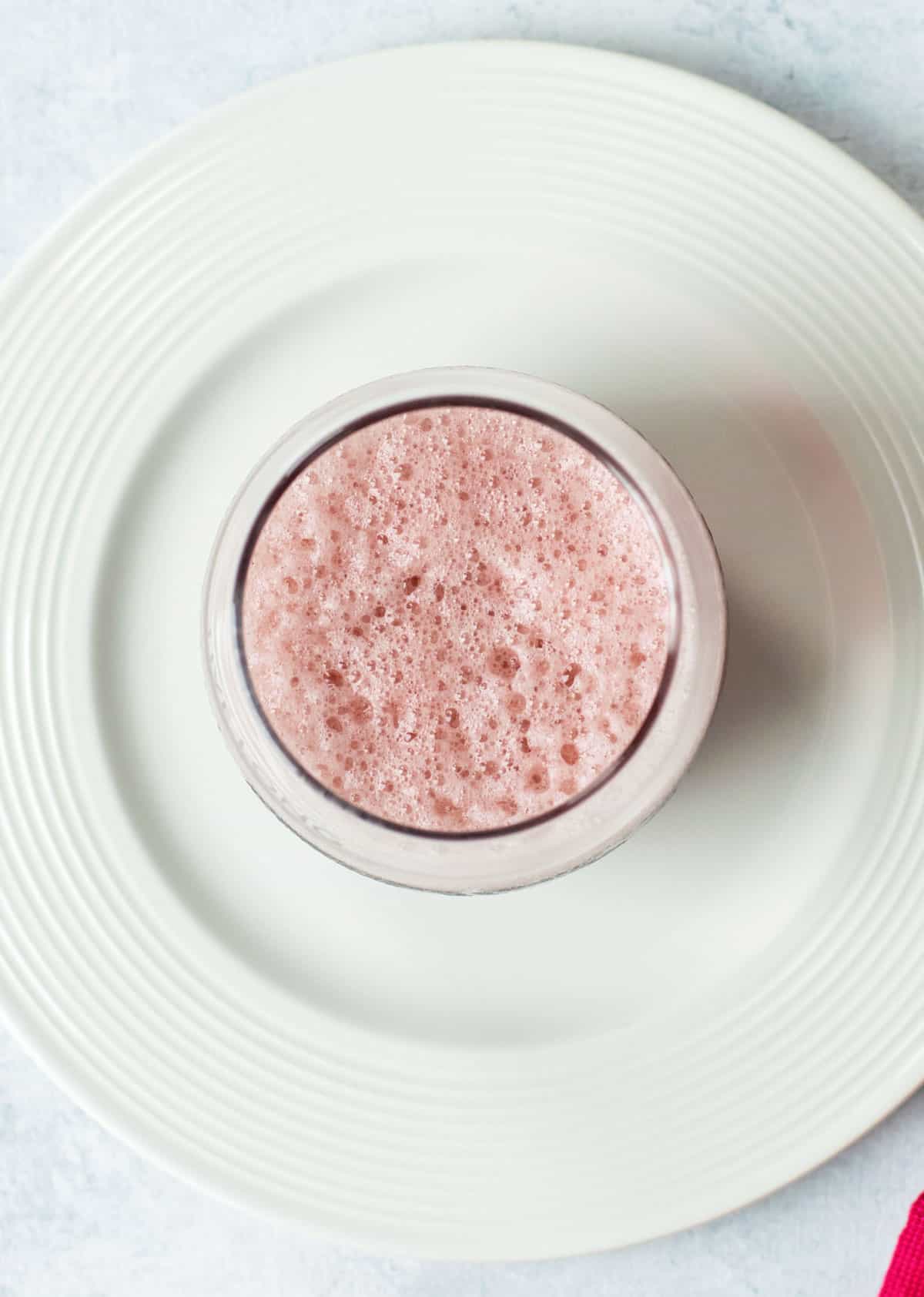 pink foamy drink in glass on white plate
