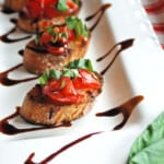 tomato bruschetta on white plater with drizzled balsamic glaze