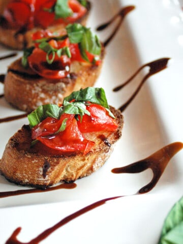 tomato bruschetta on white plater with drizzled balsamic glaze