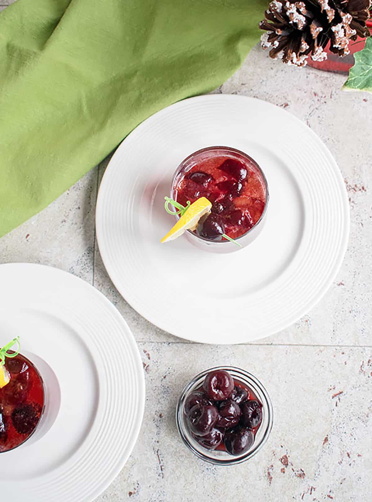 cherry cocktails on plates with lemon and cherry garnishes, bowl of dark cherries