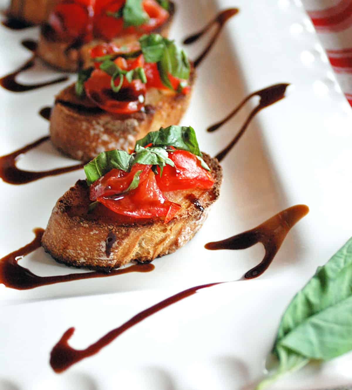 tomato bruschetta with balsamic glaze on white platter with basil