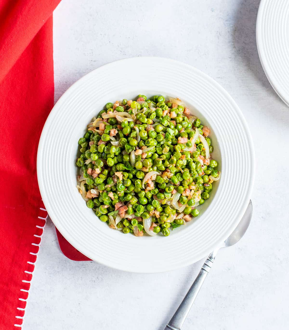 bowl of peas with onions and pancetta, red napkin, spoon