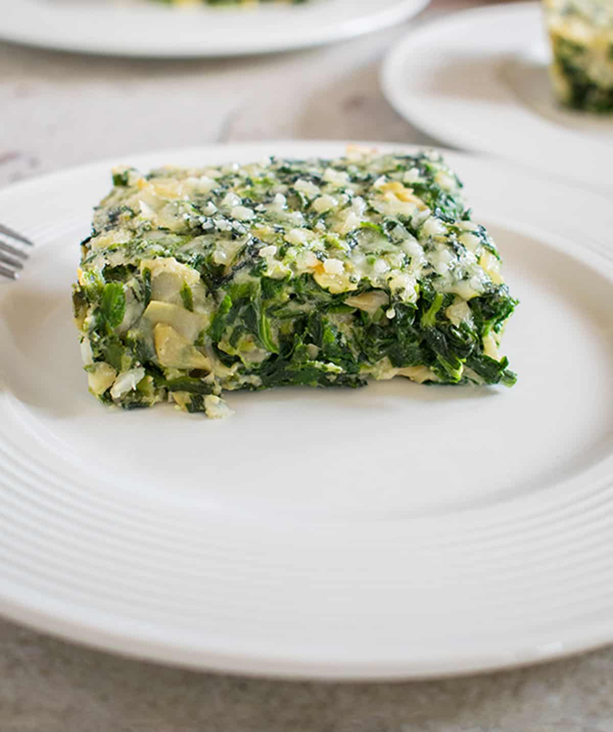 piece of spinach artichoke casserole on white plate with fork