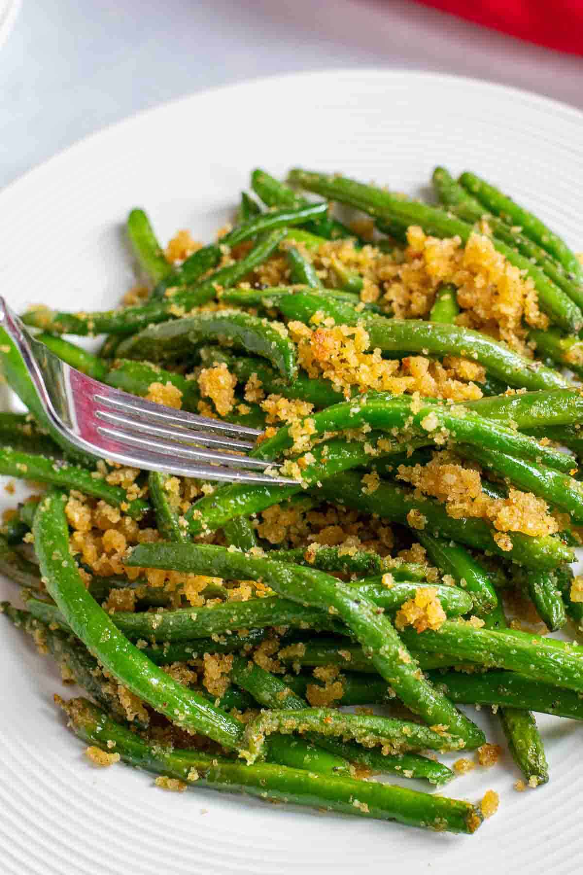 forkful of green beans with bread crumbs from a white plate