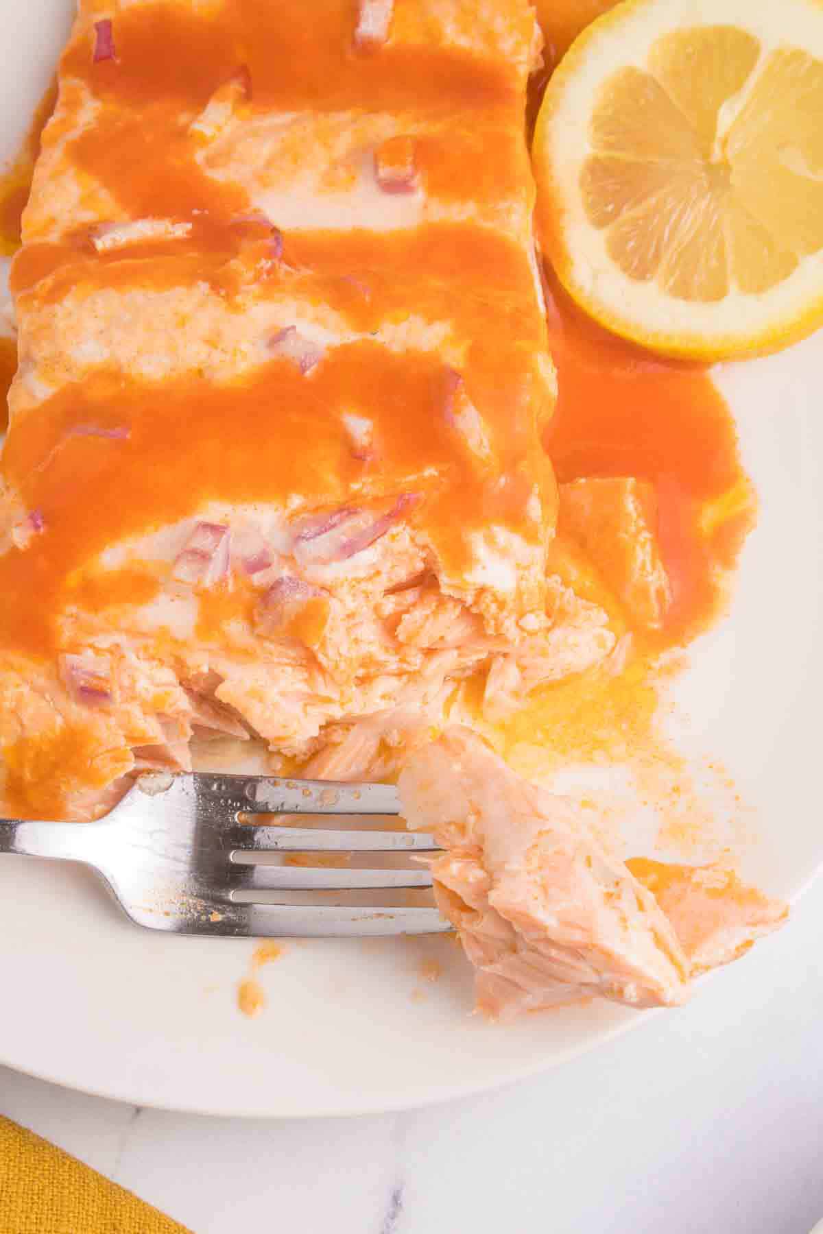 forkful of salmon from piece of salmon with Buffalo sauce and onions