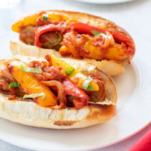 two sausage and pepper sandwiches on a plate topped with sauce and basil.