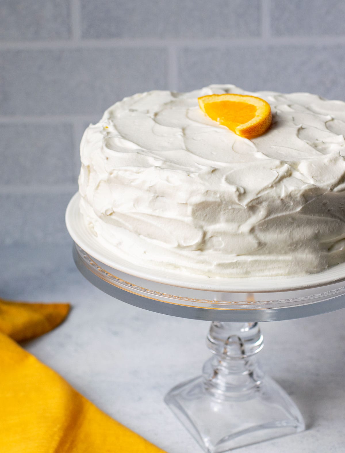 orange sponge cake with whipped cream on cake stand garnished with orange slice