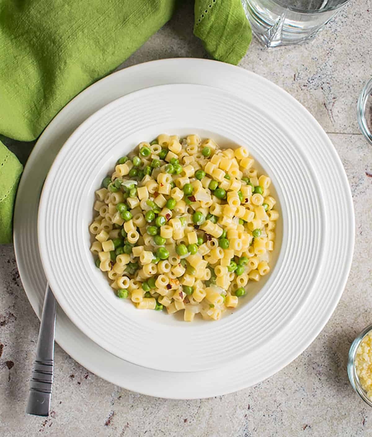 bowl of pasta with peas on white plate with green napkin
