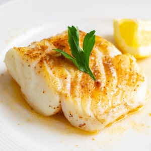 thick piece of seared cod on plate with melted butter, lemon