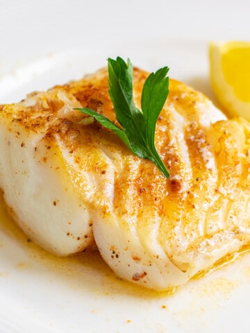 thick piece of seared cod on plate with melted butter, lemon