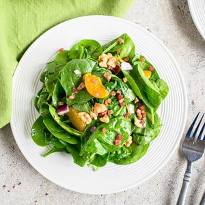 spinach salad with mandarin oranges, walnuts and pancetta on white plate