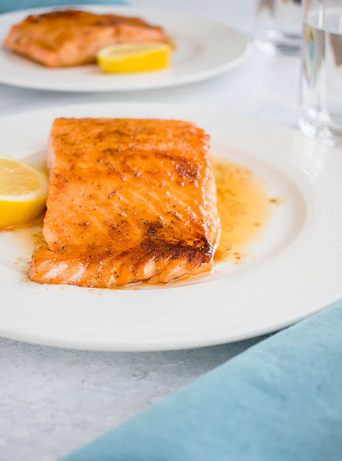 two plates of maple-glazed salmon with lemon and glasses of water