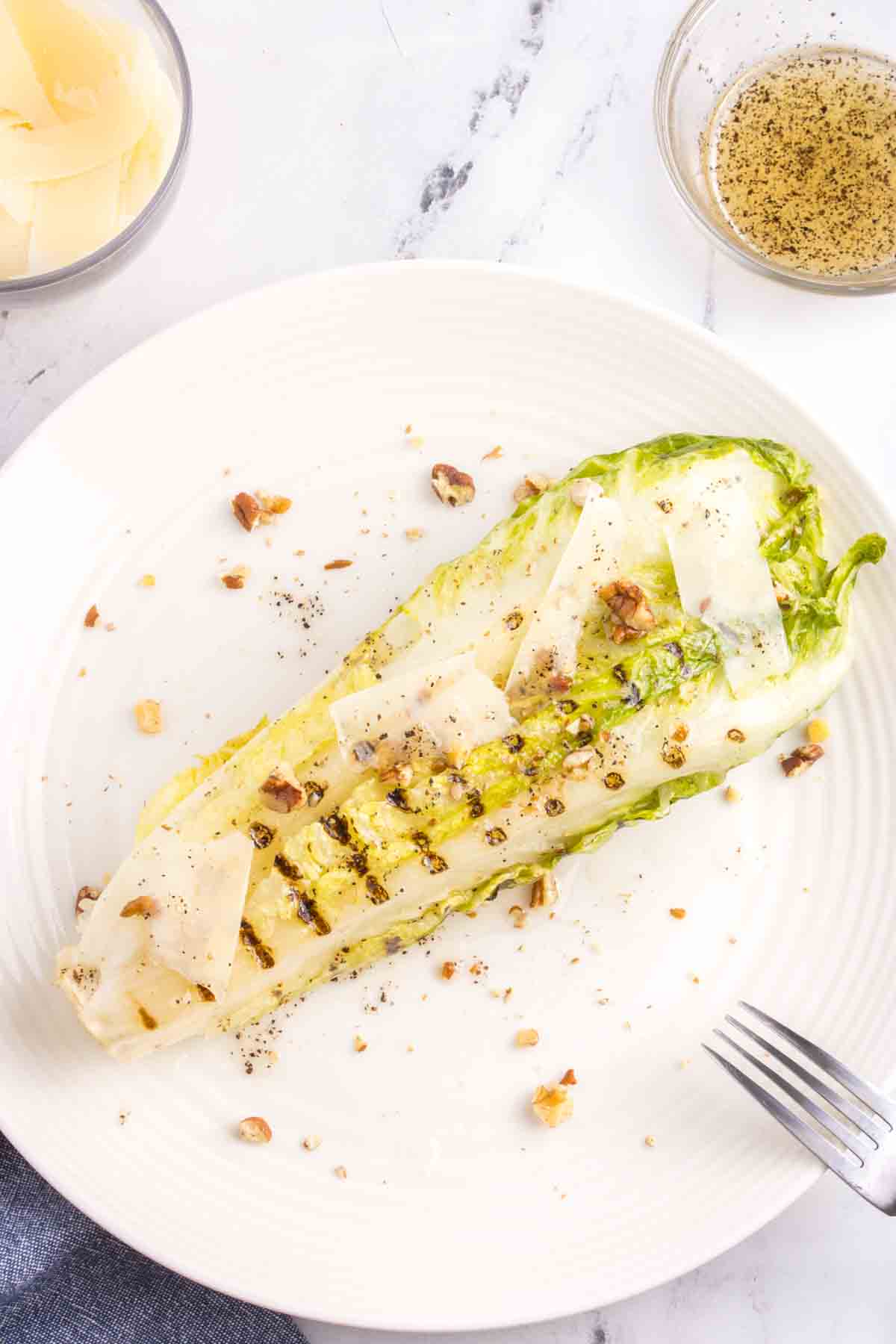 grilled romaine heart with Parmesan slivers and walnuts on plate with fork