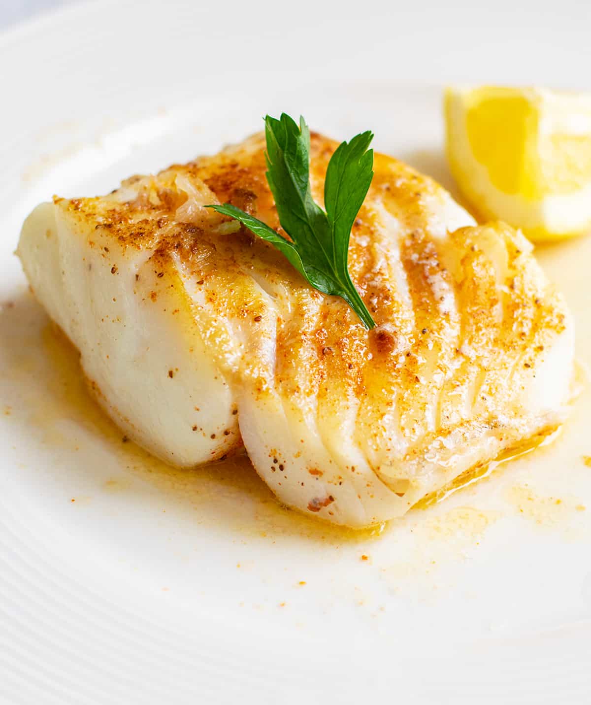 seared cod on white plate with parsley, lemon, melted butter