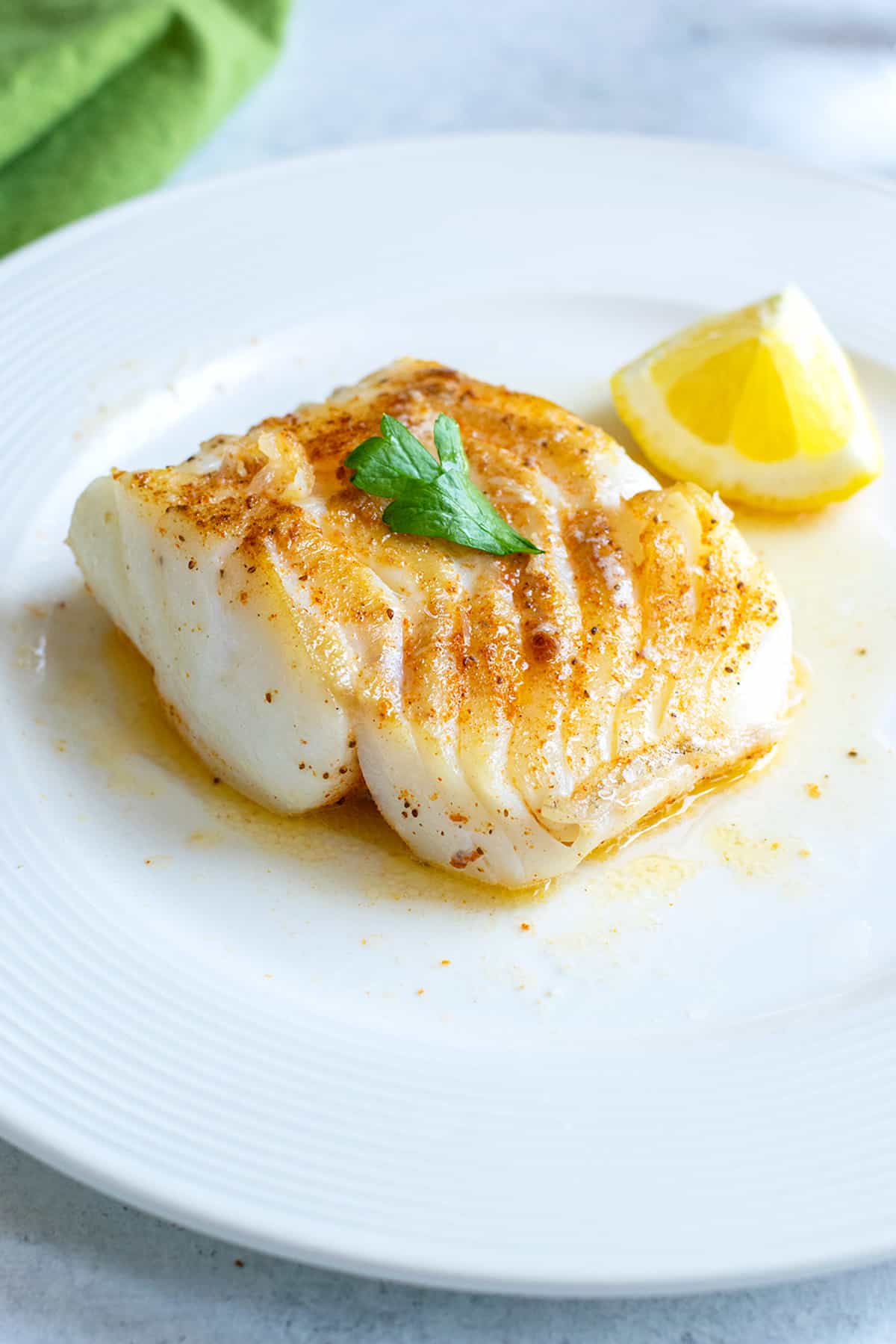 seared cod on white plate with parsley, lemon wedge and melted butter