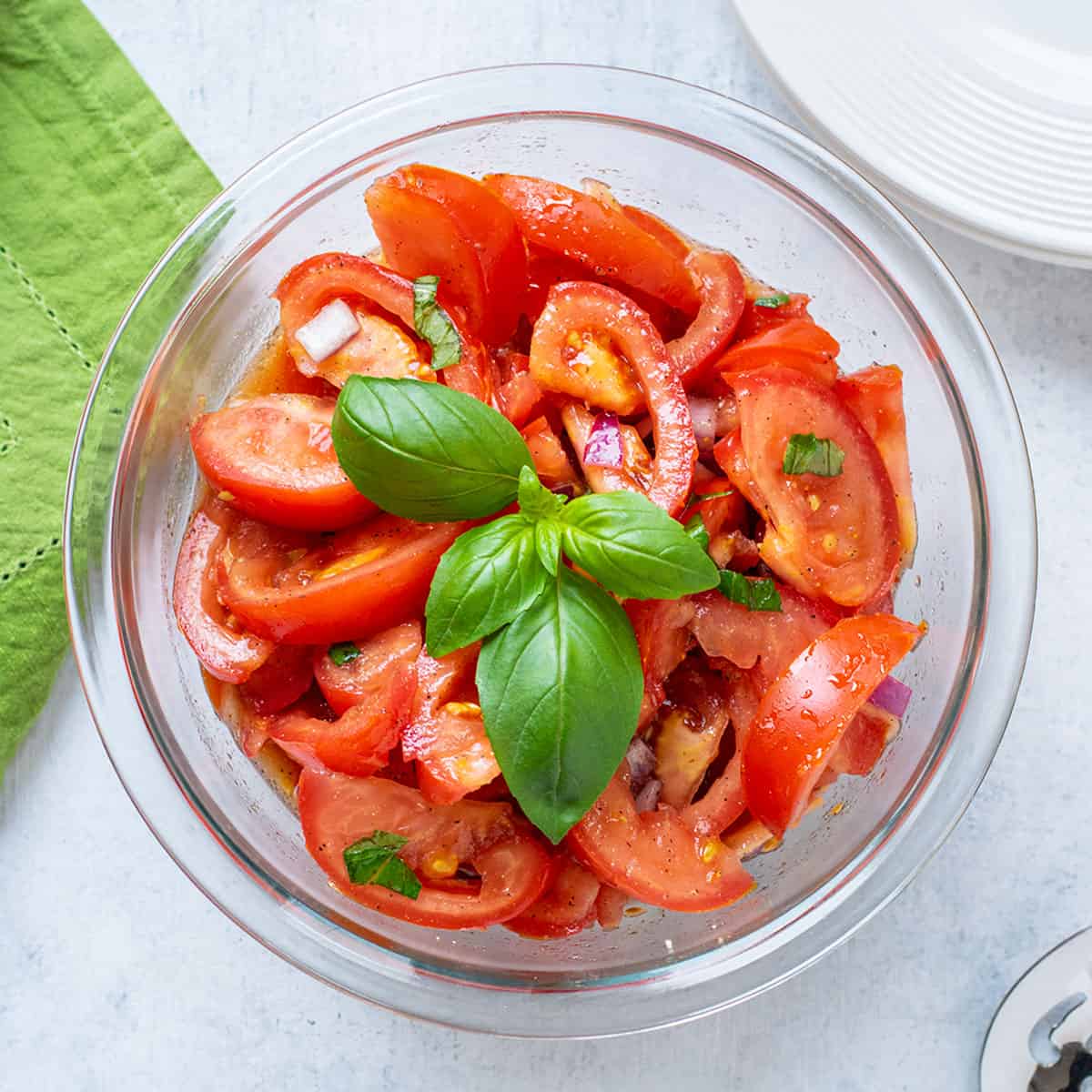 Prepared tomato salad in a glass bowl with basil on top.